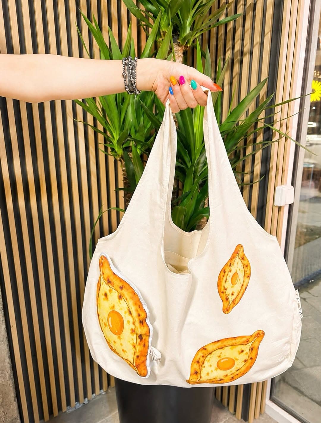 Cream canvas shopper bag covered in adjaruli khachapuri prints, with a plush khachapuri pocket